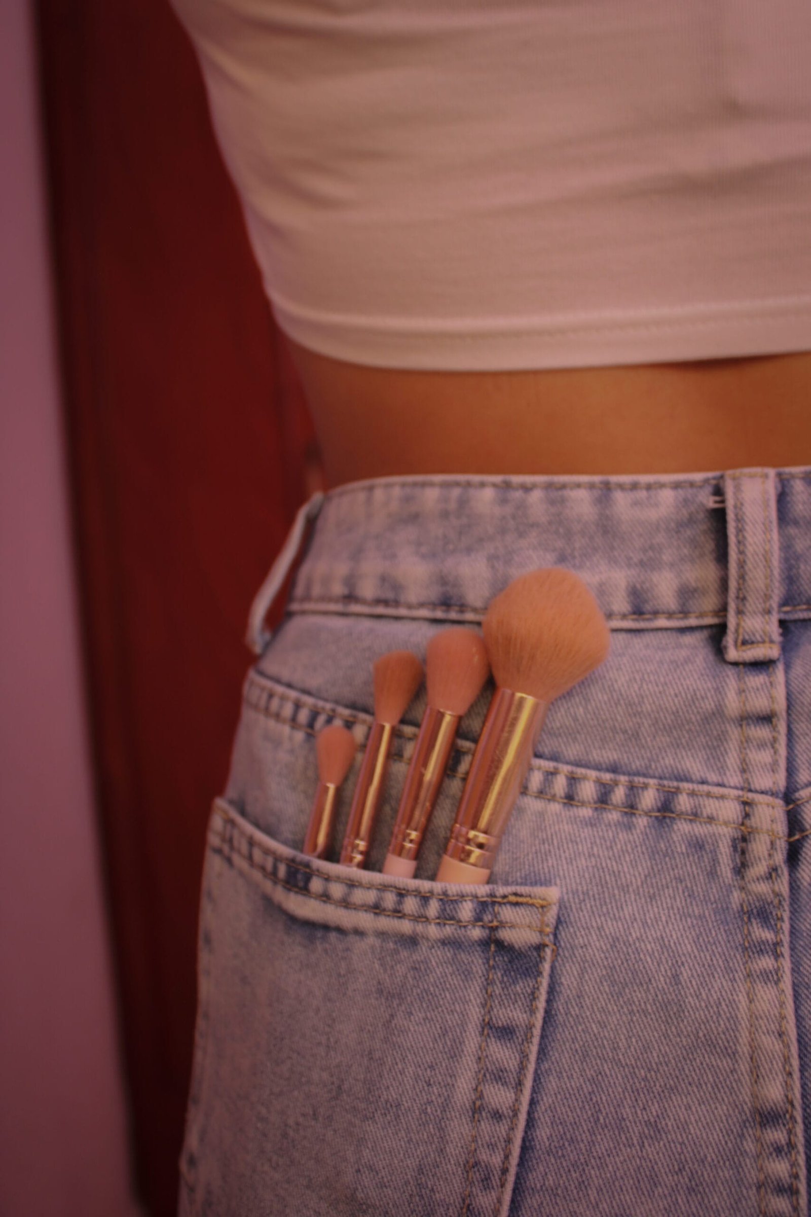Brochas de maquillaje color rosa de distintos tamaños para cualquier tipo de maquillaje dentro del bolsillo de un pantalón de mezclilla de una mujer joven