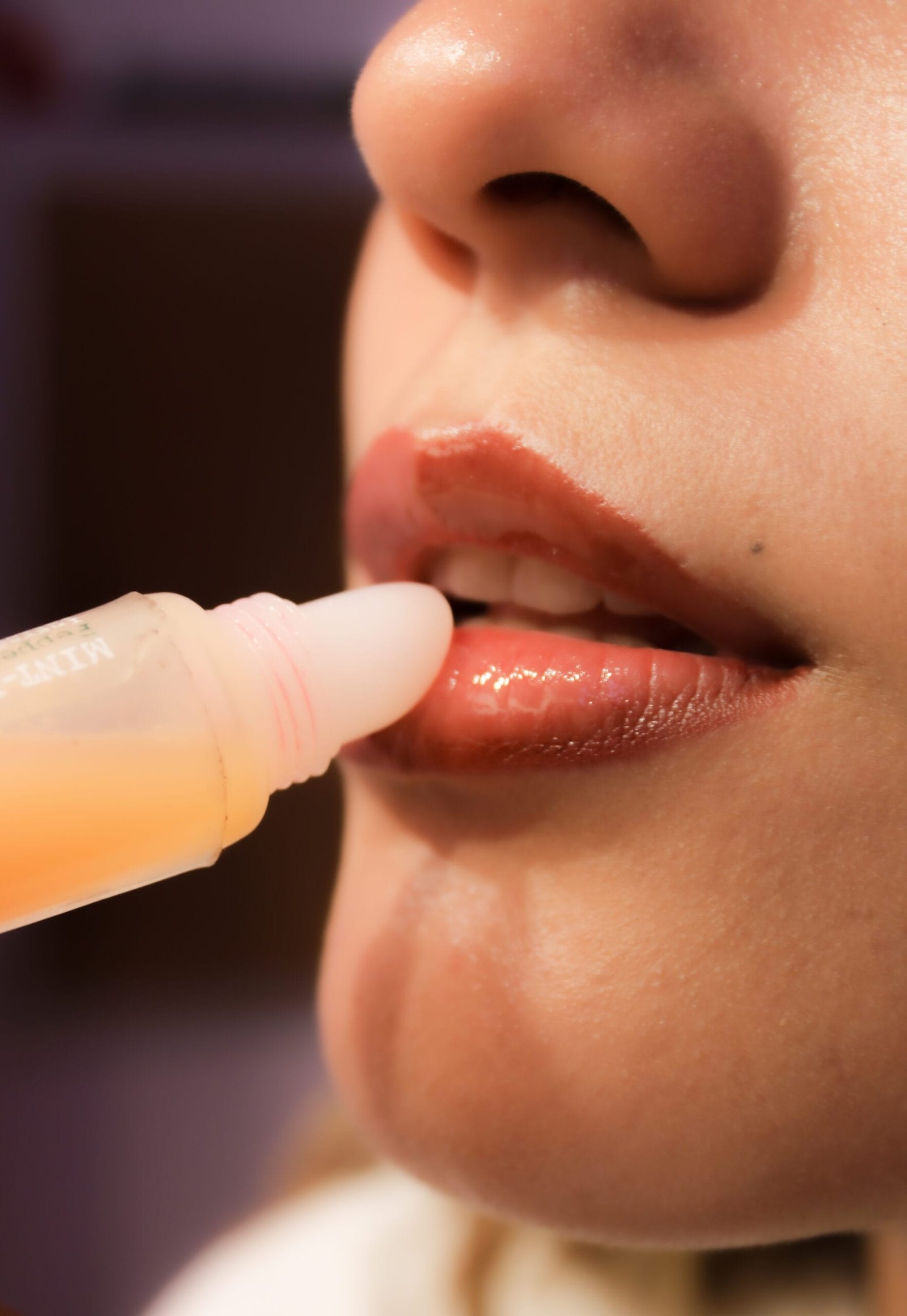 Mujer joven colocándose un gloss en color dorado en labios rojizos, con labios semi abiertos.