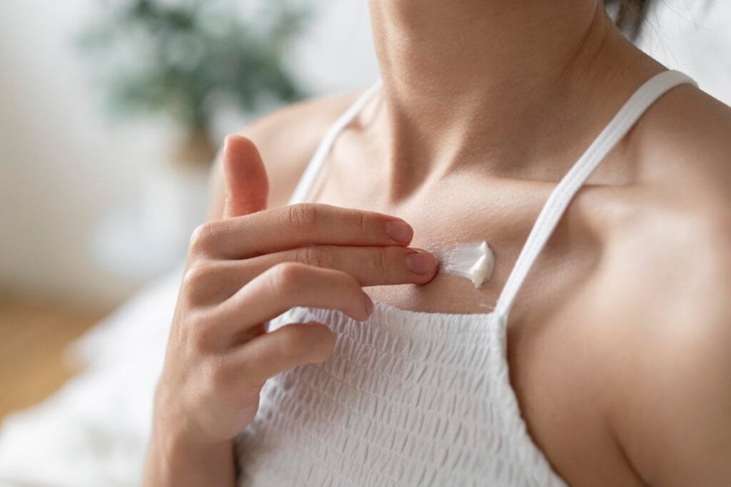 mujer aparentemente milenial con piel sana, sin texturas, sin apariencia apagada; aplicándose protector solar corporal para evitar manchas solares y protegerse de los rayos UV,UVA y UVB