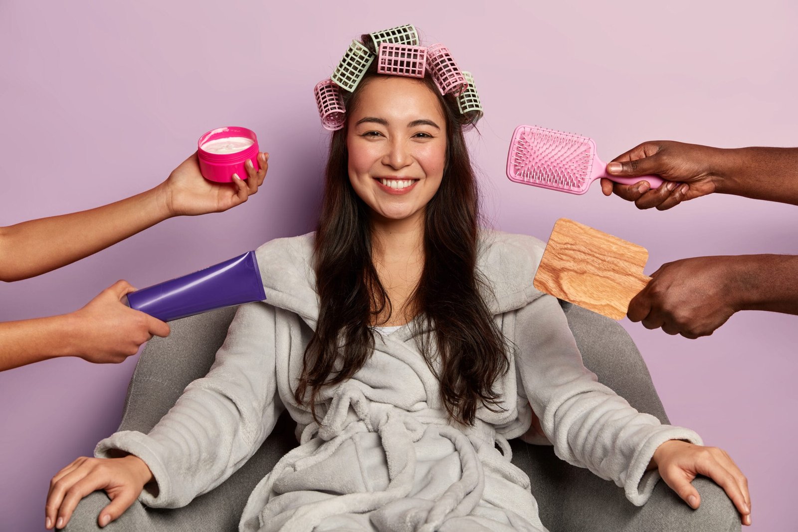 chica asiática alegre y de piel morena se riza el cabello mientras recibe una gran variedad de procedimientos cosméticos