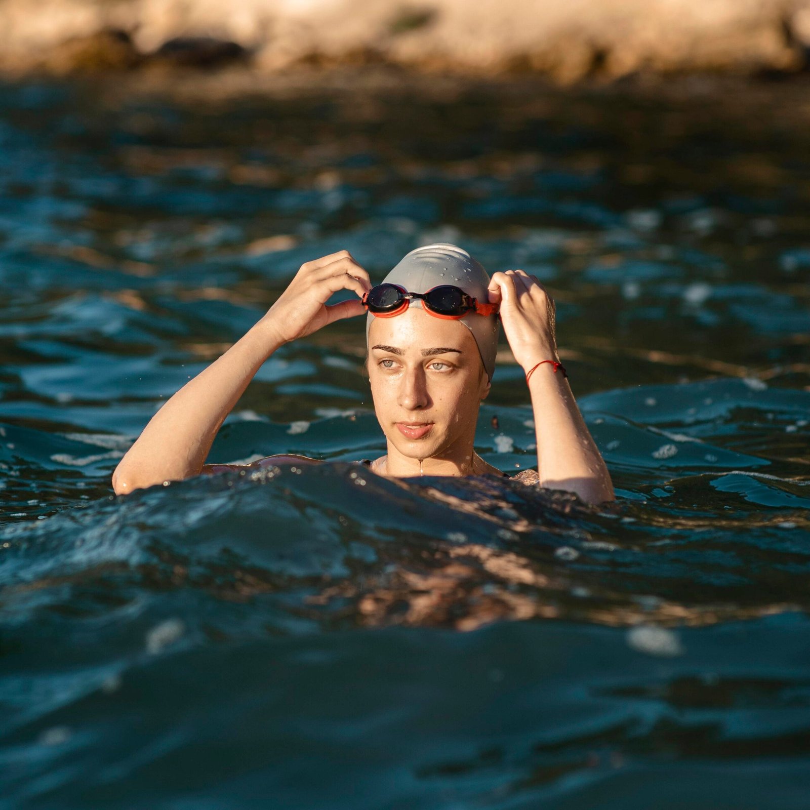chica de tez blanca se encuentra en el mar mientras usa un gorro de natación para proteger su cabello