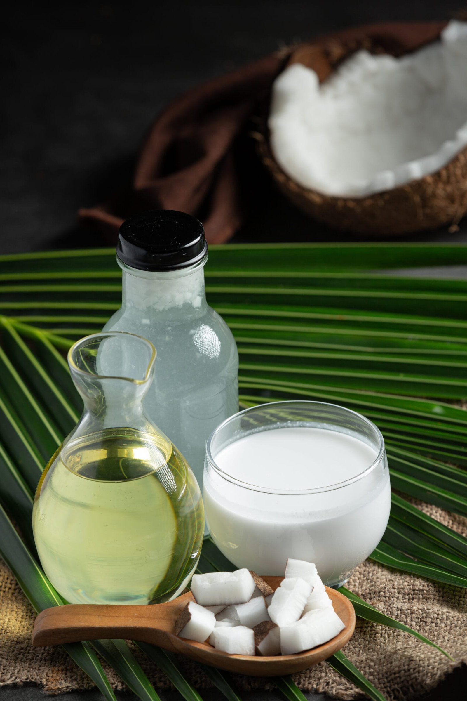 proceso de la extracción del aceite de coco, mostrando frascos con los ingredientes y una cuchara con el coco cortado, todo extraído de forma natural, situado en una hoja natural y verde aceite de coco natural extraído del coco, posicionado sobre una hoja reflejando la naturaleza