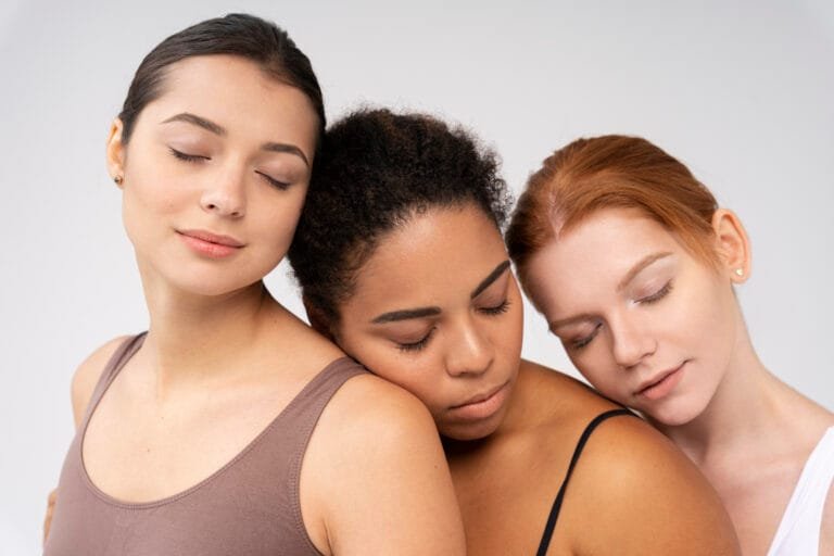 Tres mujeres con diferentes tonos de piel recostadas juntas con los ojos cerrados, en gesto de calma y conexión.