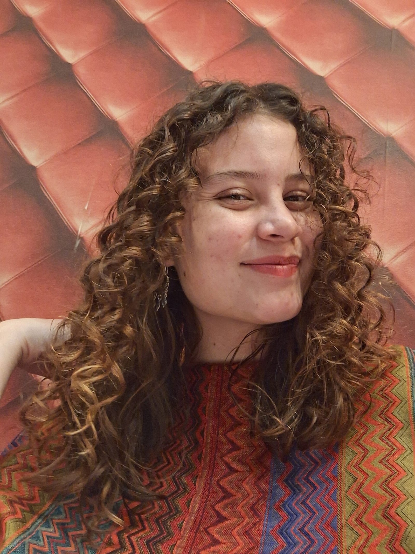 mujer sonriente con cabello chino 3 a, blanca, rubia oscura, son método plopping, rizos poco definidos y poco volumen, cejas poco marcadas, con poco pelo, aretes largos, vestida con prenda mexicana