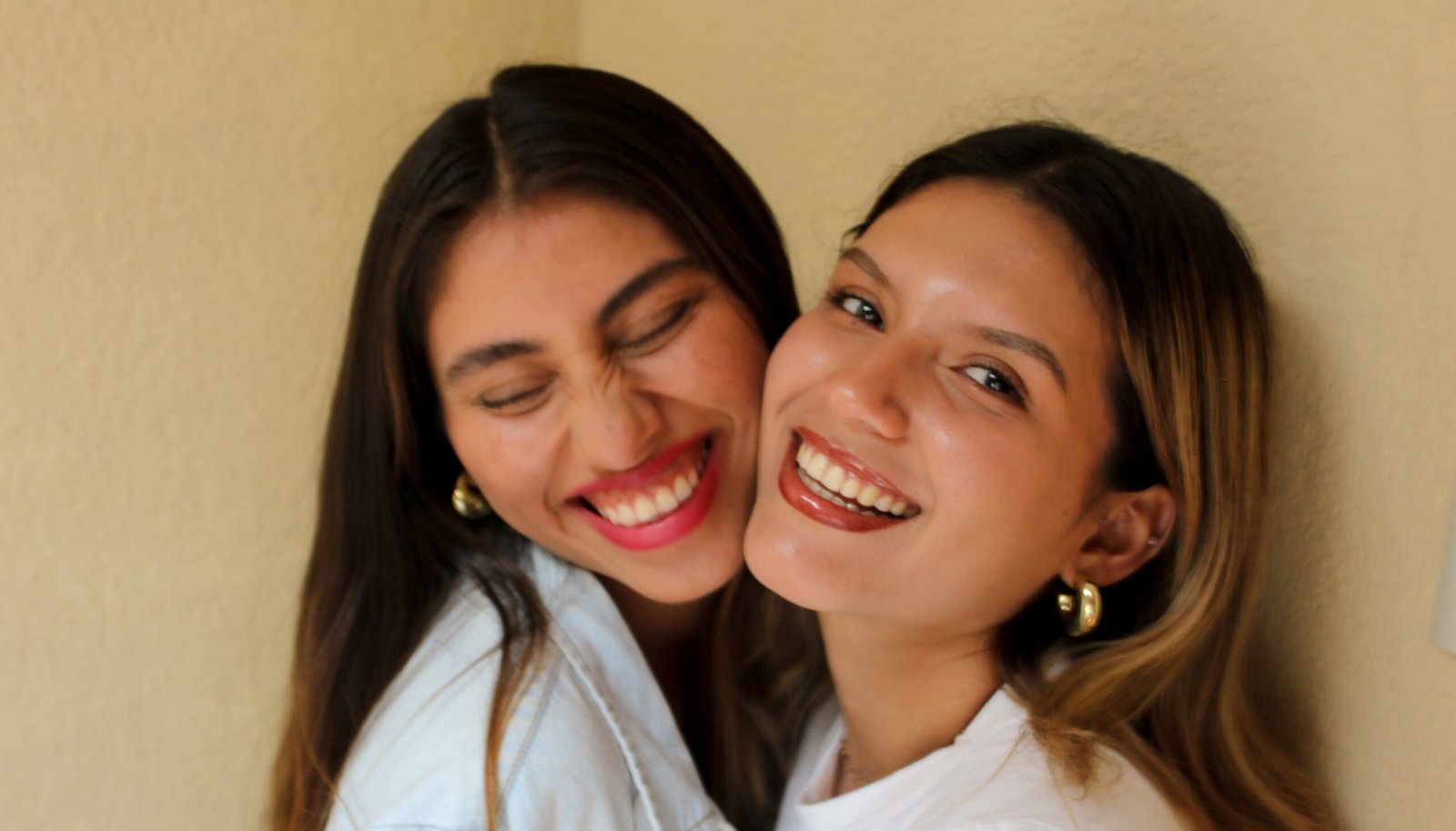 Mujeres jovenes exitosas, con rostro sonriente, aretes dorados, rubia y castaña, mostrando sus dientes, con ojos oscuros, maquillaje sencillo, gloss y fondo amarillo.