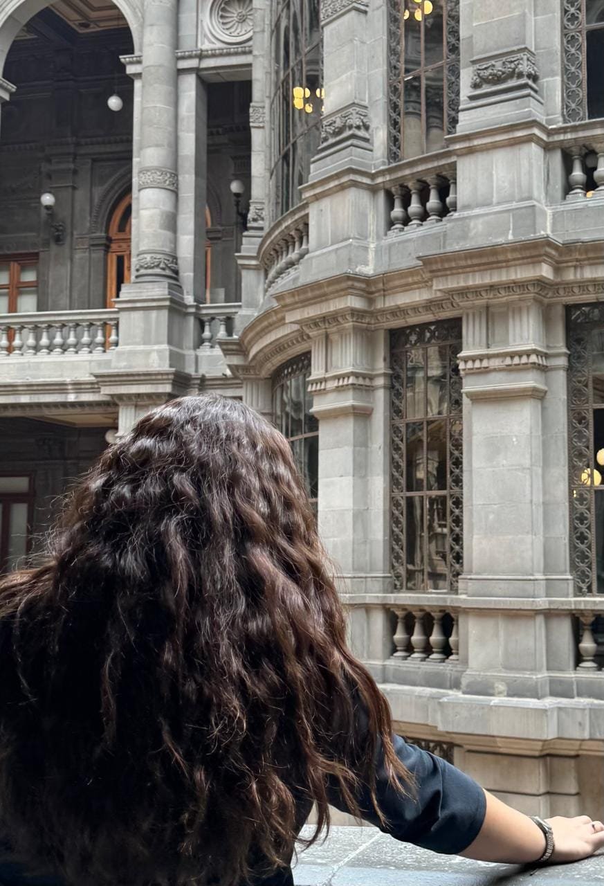 mujer mostrando su cabello ondulado 2c, de cabellera larga, castaña, con mucho cabello y volumen desde la raíz, con fondo estructural antiguo y rústico francés
