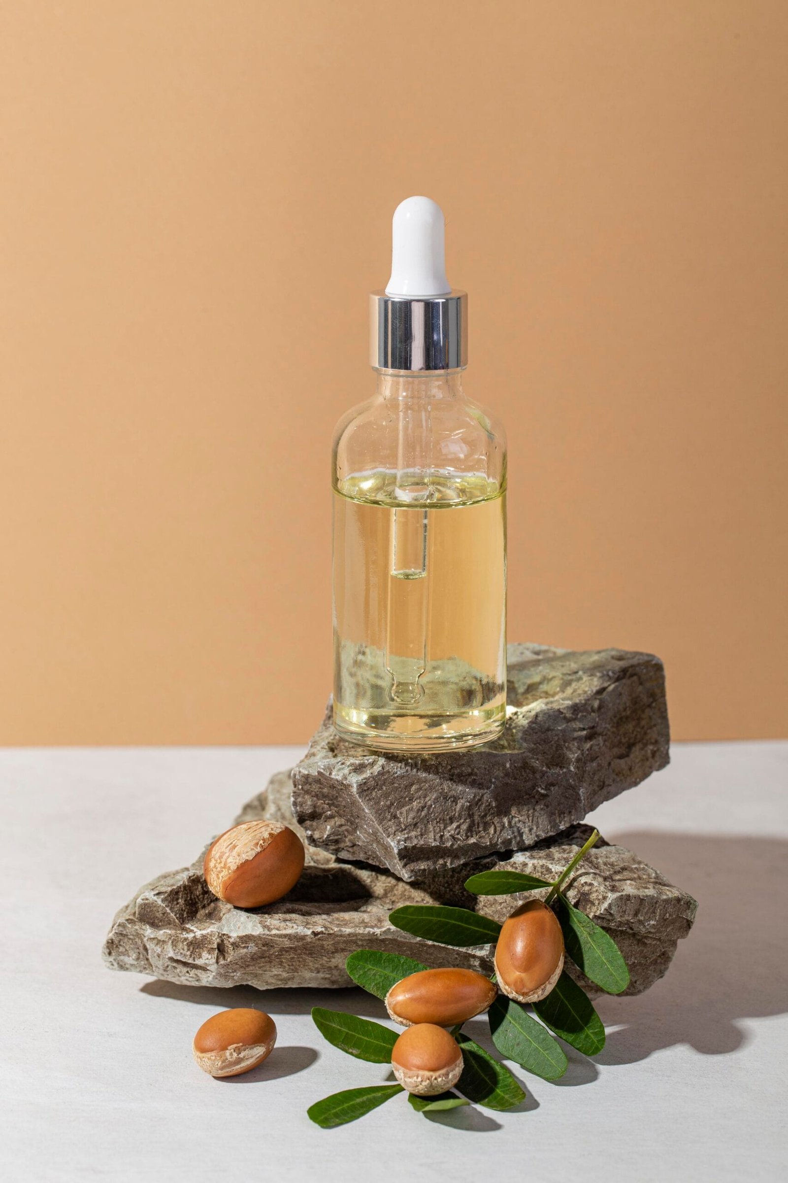 gotero con aceite de argán para el crecimiento del cabello, colocado sobre piedras y algunas semillas encima