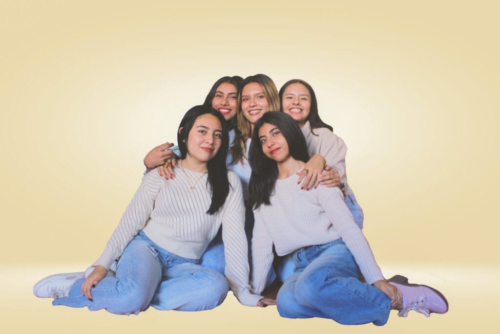 Cinco mujeres sonrientes en ropa deportiva posando juntas frente a un fondo amarillo vibrante.